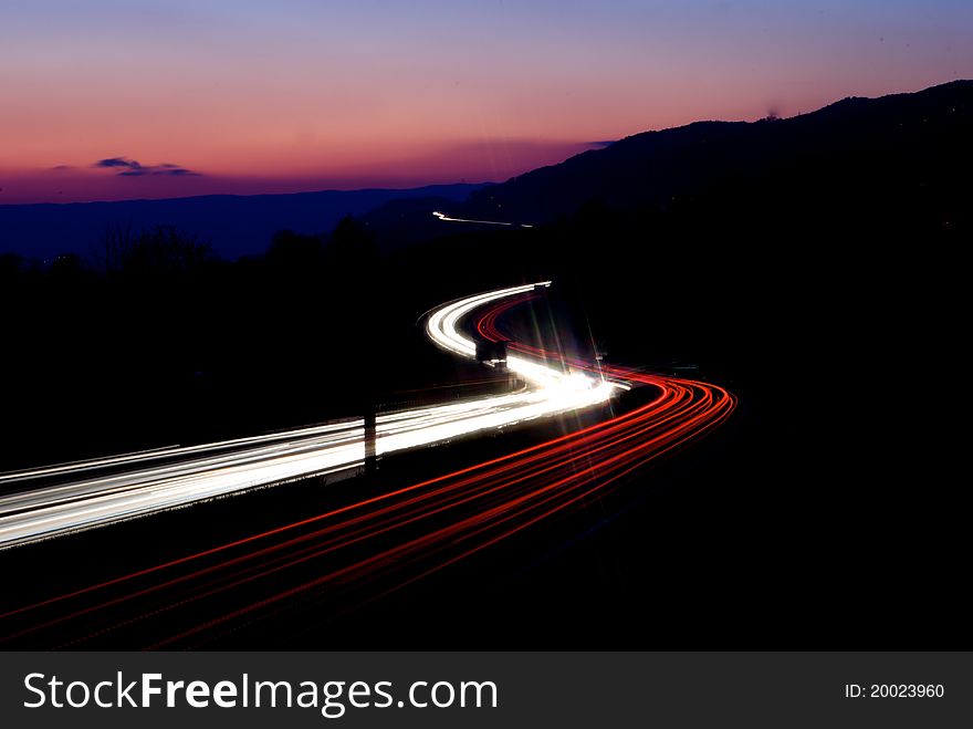 Highway with car trails in front of sunset