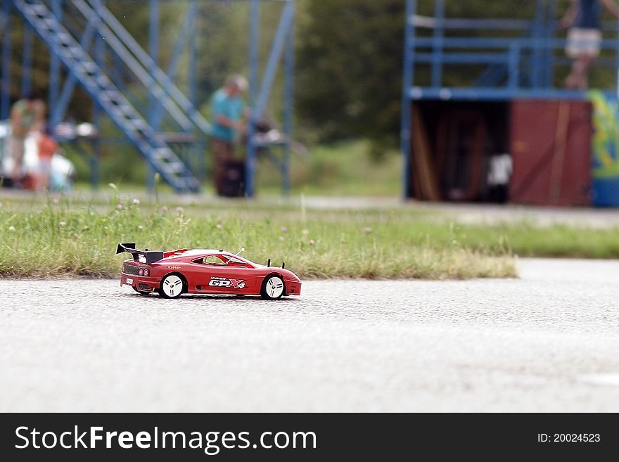 Remote-controlled toy car while driving on the track model. In the background there are modelers.