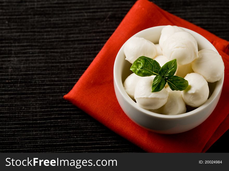 Photo of delicious small mozzarella cherries with basil inside a bowl. Photo of delicious small mozzarella cherries with basil inside a bowl
