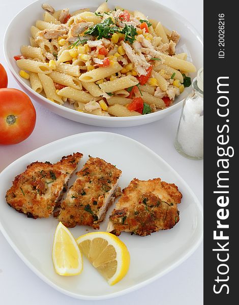 A plate of Chicken Milanese with lemon wedges and a plate of chicken pasta. A plate of Chicken Milanese with lemon wedges and a plate of chicken pasta