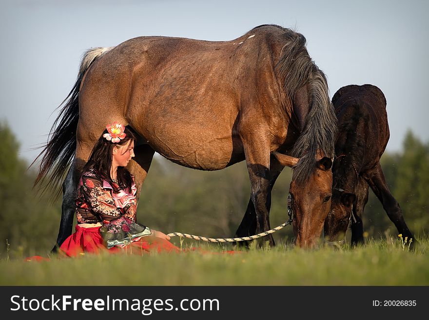 A gypsy-dressed girl sits near her horses in the field at sunset. A gypsy-dressed girl sits near her horses in the field at sunset.