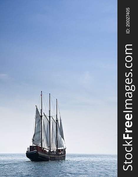 A large sail boat carrying passengers and sailing off toward horizon on a summer's day. A large sail boat carrying passengers and sailing off toward horizon on a summer's day.