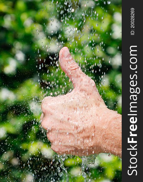 Thumbs up under falling water on a green background