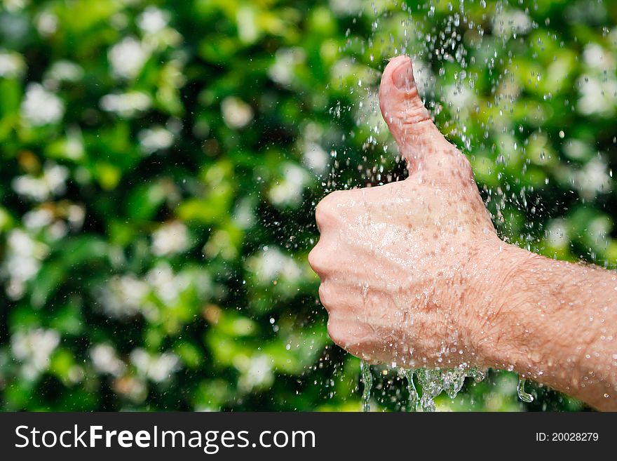 Thumbs up under falling water on a green background