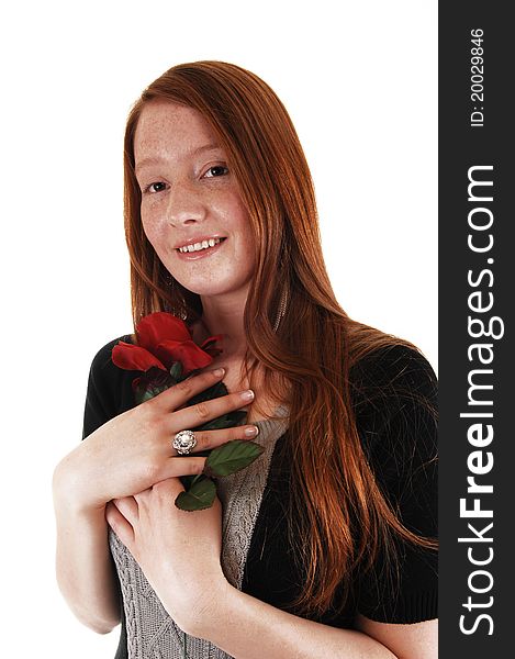 A young woman with long red hair holding a red rose close to her chest and smiling into the camera, for white background. A young woman with long red hair holding a red rose close to her chest and smiling into the camera, for white background.