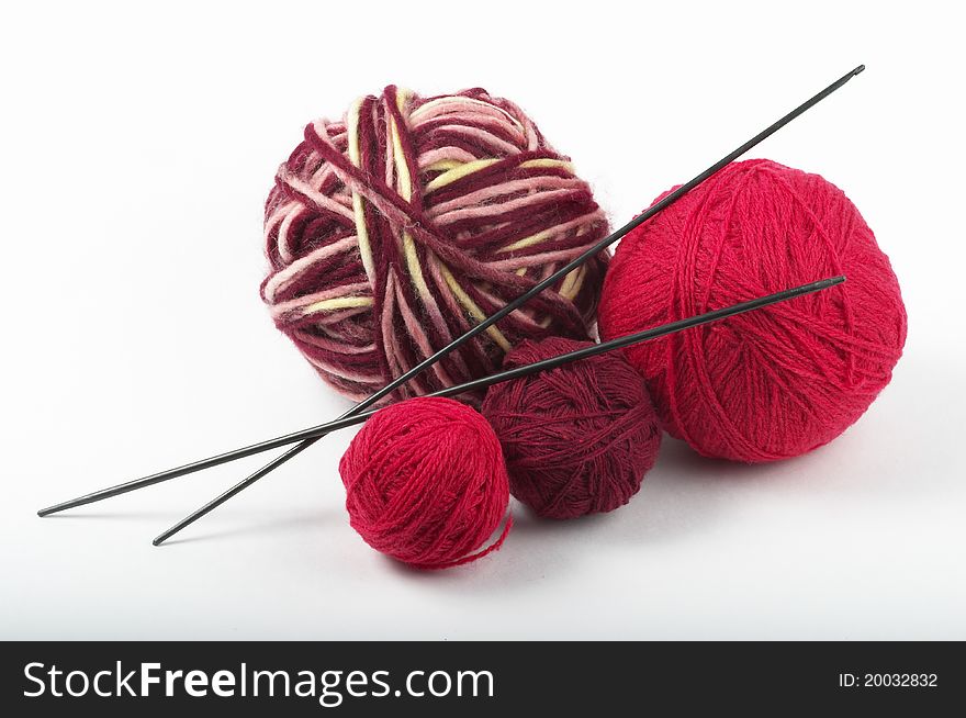 Four colored wool clews stack and knitting needles over grey background