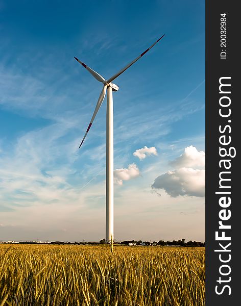 A wind turbine in the grain-field in front of blue sky. A wind turbine in the grain-field in front of blue sky