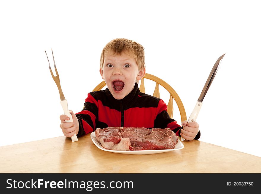 A young boy with a happy expression on his face with a large steak on his plate holding a big knife and big fork. A young boy with a happy expression on his face with a large steak on his plate holding a big knife and big fork.