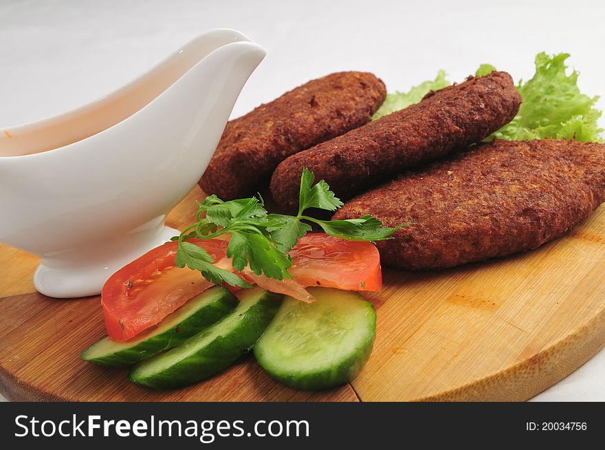 The fried cutlets with sauce and vegetables on a round board