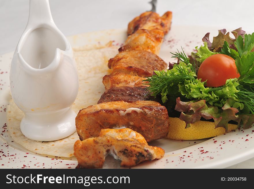 Meat from a brazier with sauce and a garnish on a white plate