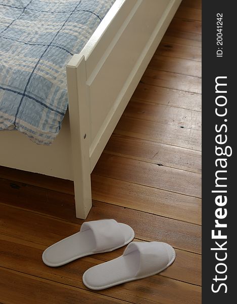 Pair of white slippers in hotelroom in front of corner of bed