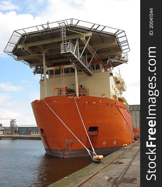 An orange offshore support vessel moored to a quay. An orange offshore support vessel moored to a quay