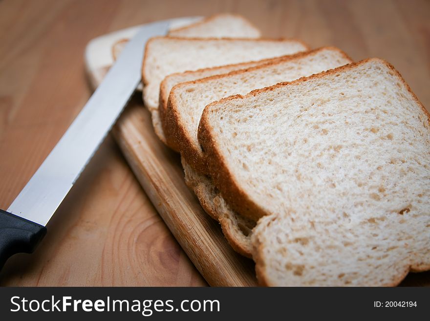 Sliced bread with knife, on cutting board.