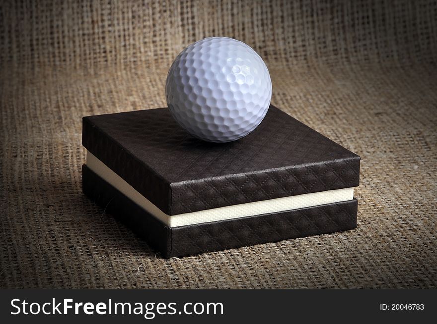 A golf ball on a brown box, photographed in a studio.