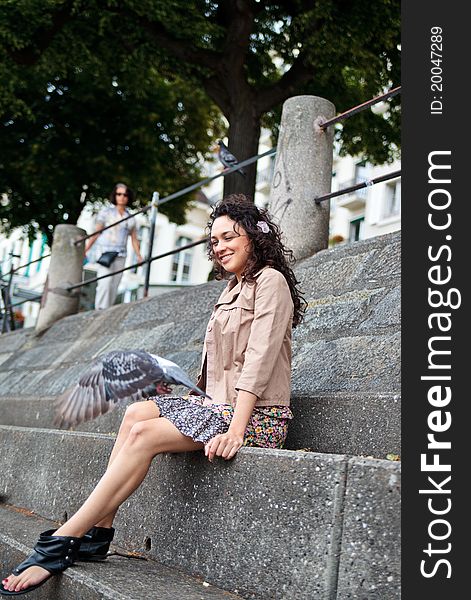 Portrait of young beautiful attractive woman, hispanic, Latina sitting on a stairs and looking at flying pigeon. Portrait of young beautiful attractive woman, hispanic, Latina sitting on a stairs and looking at flying pigeon