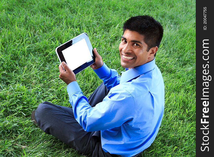 Happy young businessman sitting down on grass and holding digital tablet. Happy young businessman sitting down on grass and holding digital tablet