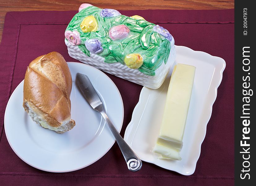 Bread on a plate and Butter in a butter dish on a placemat and wooden table. Bread on a plate and Butter in a butter dish on a placemat and wooden table.