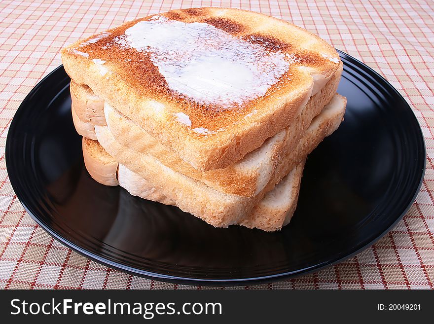 Toasted white bread with butter on a black plate. Toasted white bread with butter on a black plate.