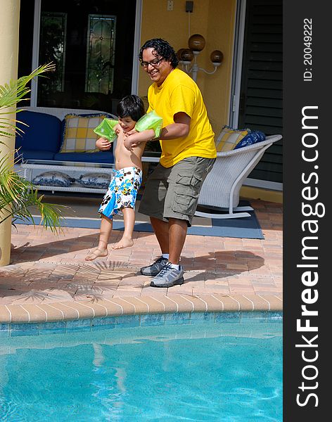 A Hispanic father throws his son into the pool. A Hispanic father throws his son into the pool