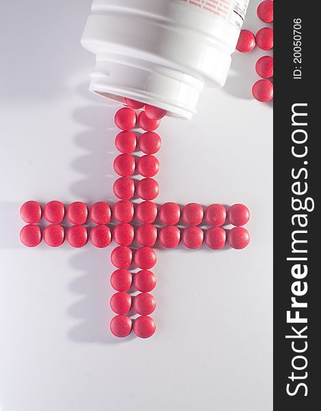 A pile of red pills scattered in the shape of cross on a white background