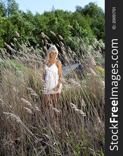 Girl in white dress are standing in dry grass at summer daylight. Girl in white dress are standing in dry grass at summer daylight