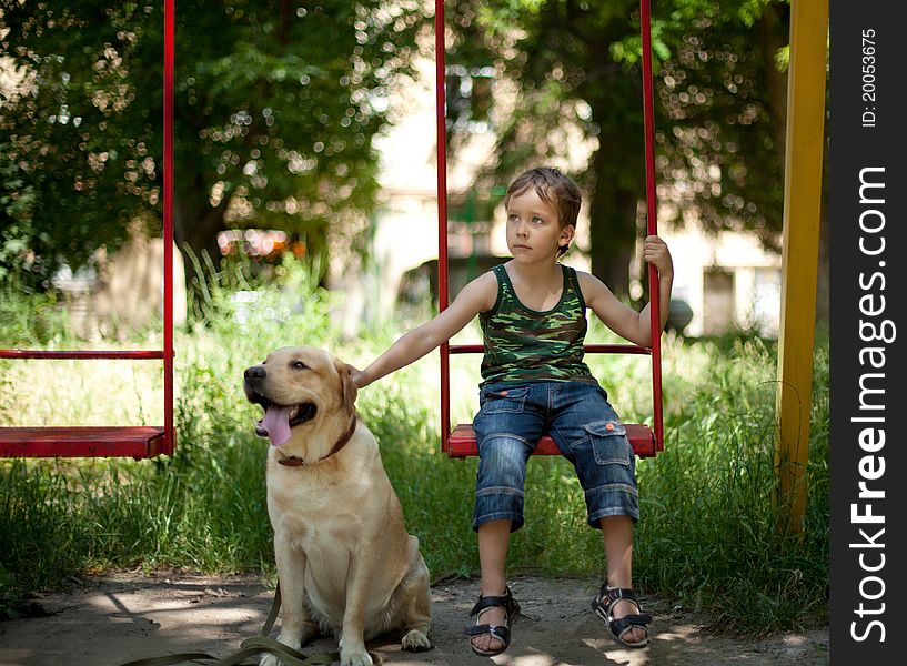 Little boy sitting on a swing with his dog