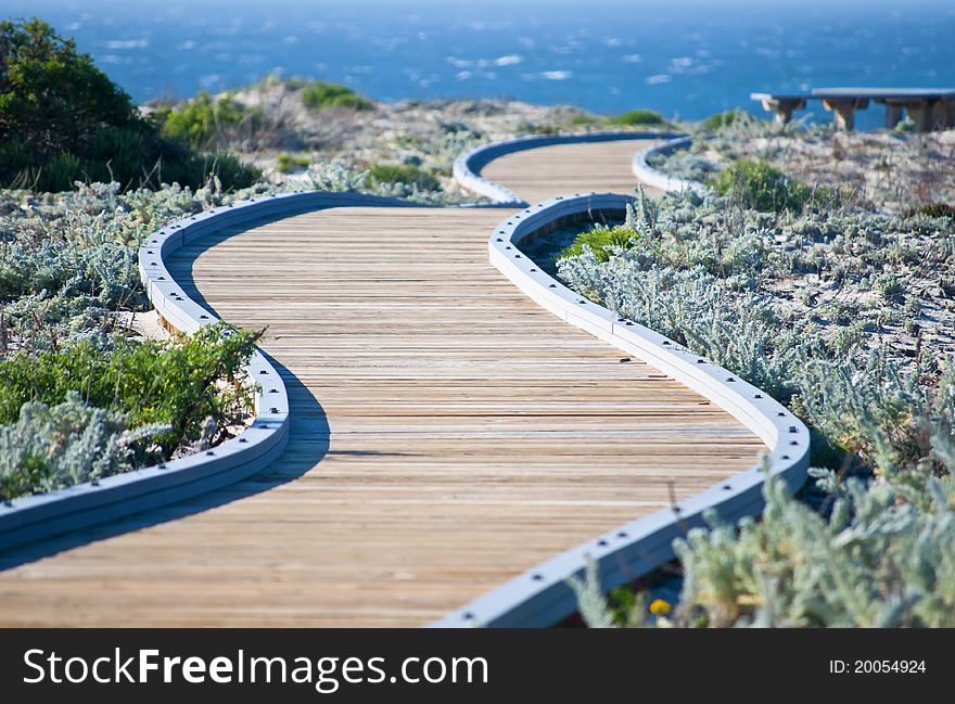 Winding wooden walkway leading towards the ocean with a bench