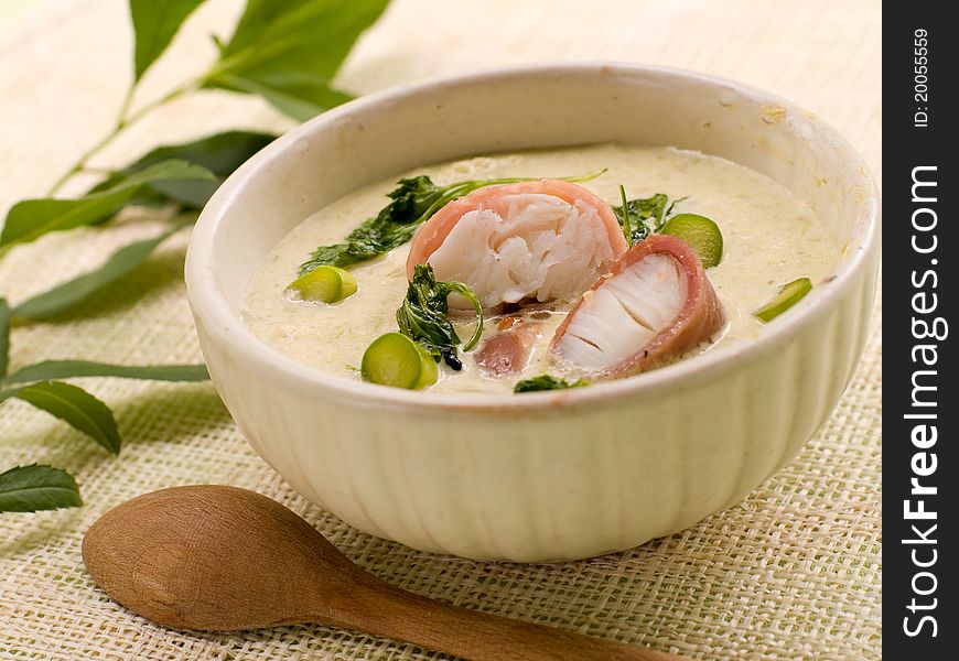 A bowl of asparagus creamy soup with fish, bacon and parsley