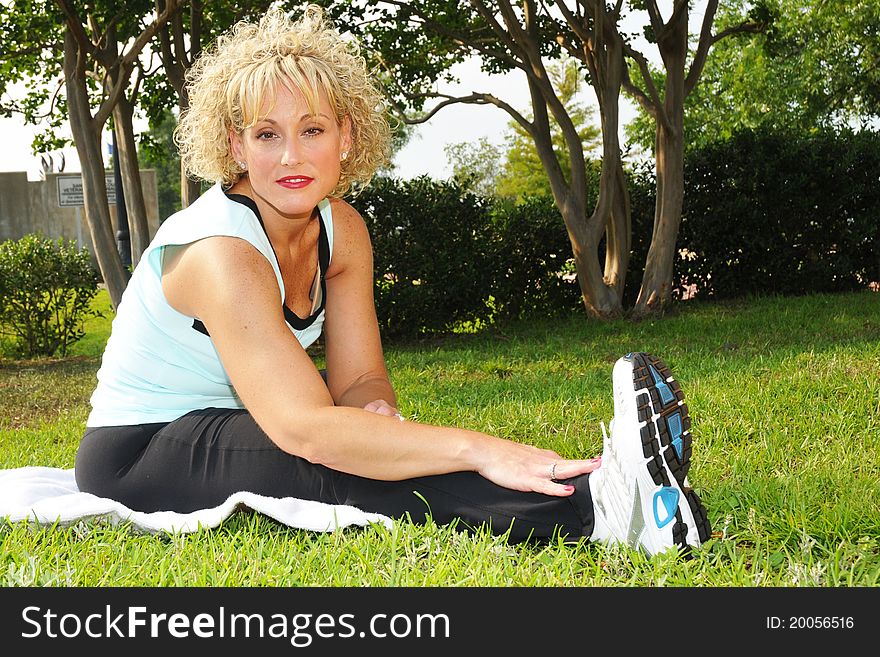 Adult woman sitting in grass with exercise clothes stretching. Adult woman sitting in grass with exercise clothes stretching