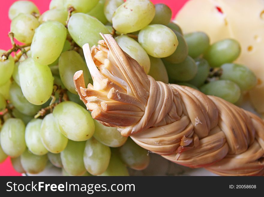 White grapes and dense smoked cheese on a red background. White grapes and dense smoked cheese on a red background