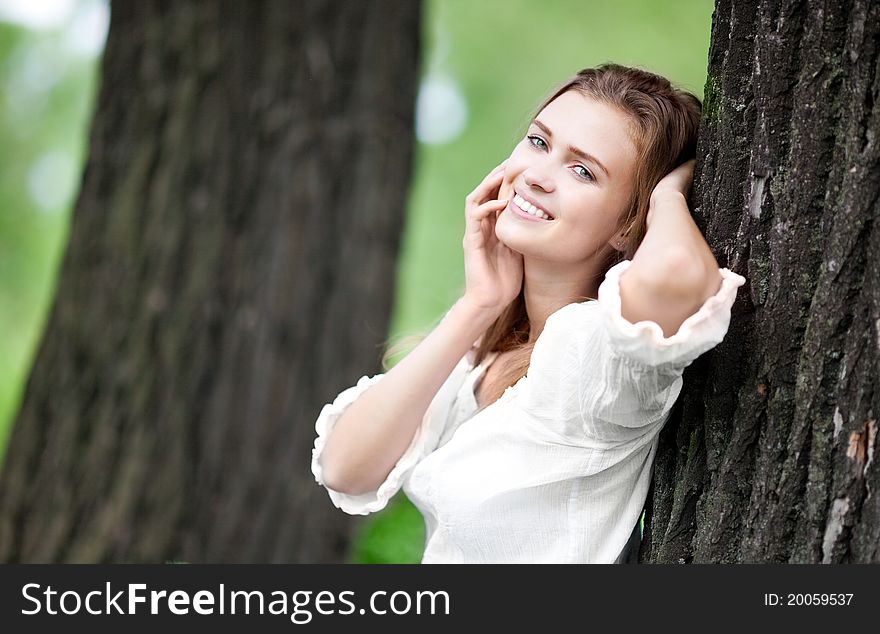 Happy young woman standing near the tree in the park on a warm summer day. Happy young woman standing near the tree in the park on a warm summer day