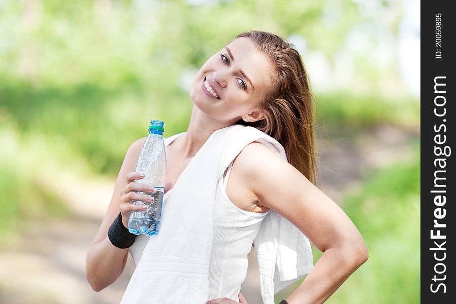 Beautiful young  sporty woman running in the park on a warm summer day and drinking water