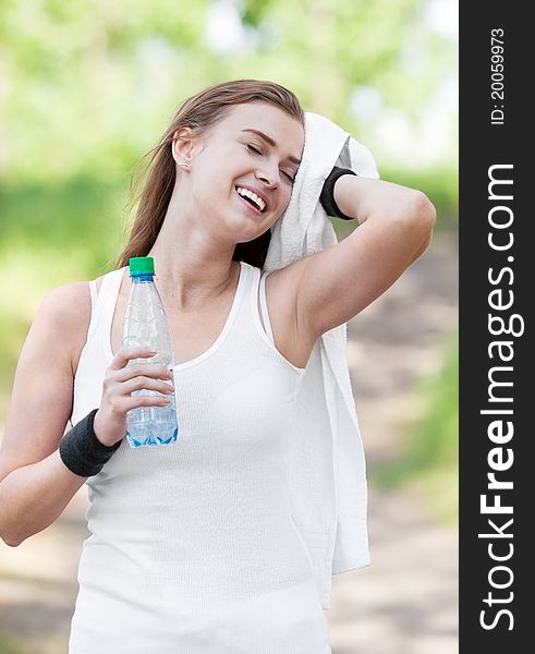 Beautiful young sporty woman running in the park on a warm summer day and drinking water