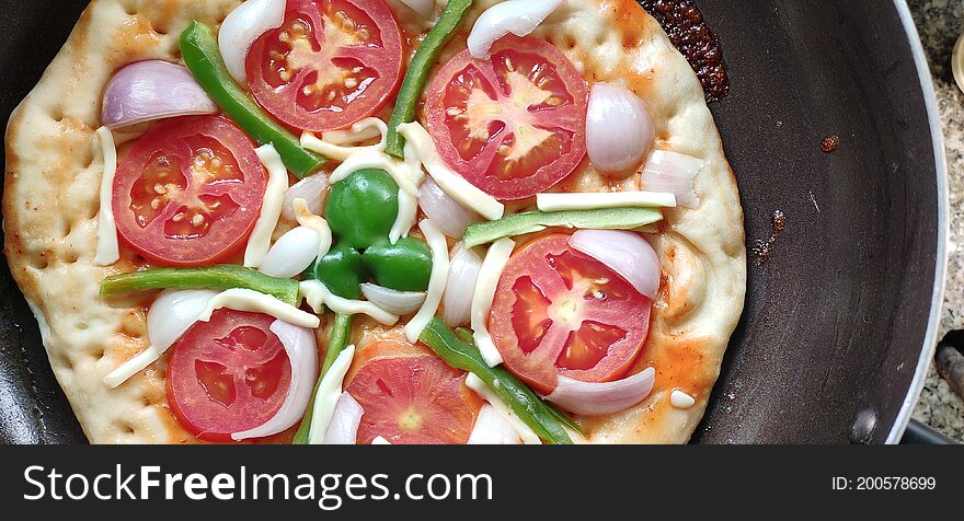 Top view of Indian home made pizza cream and dark golden brown color decorated with tomato, capsicum, cheese being cooked.