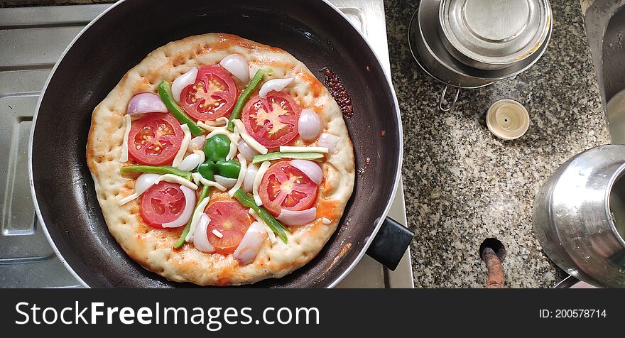 Top view of Indian home made pizza cream and dark golden brown color decorated with tomato, capsicum, cheese being cooked.