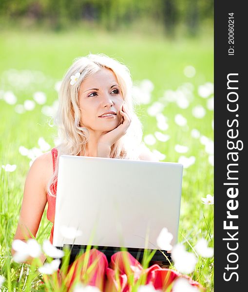 Beautiful young blond woman with a laptop  in the park  on a warm summer day