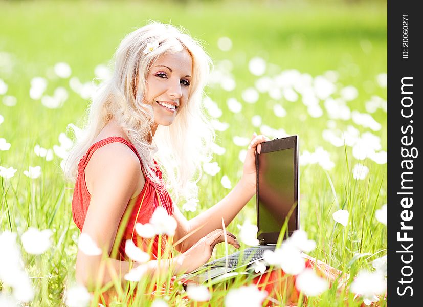 Beautiful young blond woman with a laptop  in the park  on a warm summer day