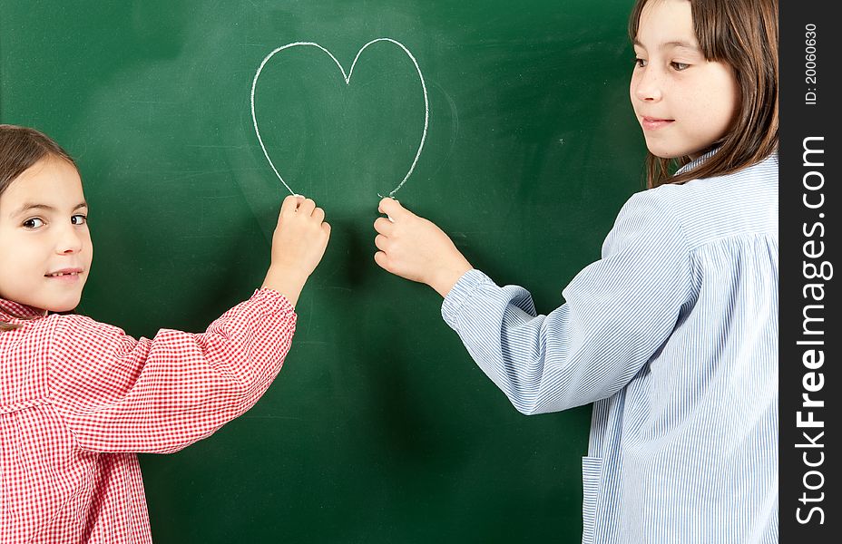Two girls drawing a heart on a green blackboard. Two girls drawing a heart on a green blackboard