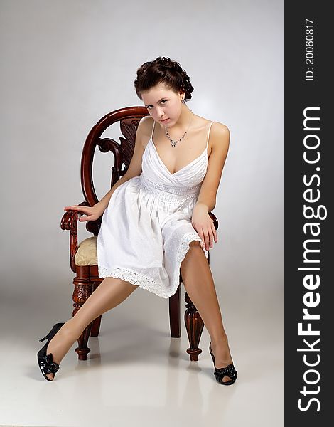 In dress sitting on chair on gray background. In dress sitting on chair on gray background