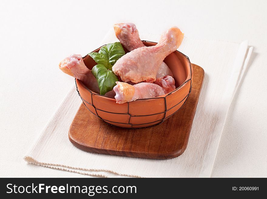 Raw chicken drumsticks in a terracotta bowl