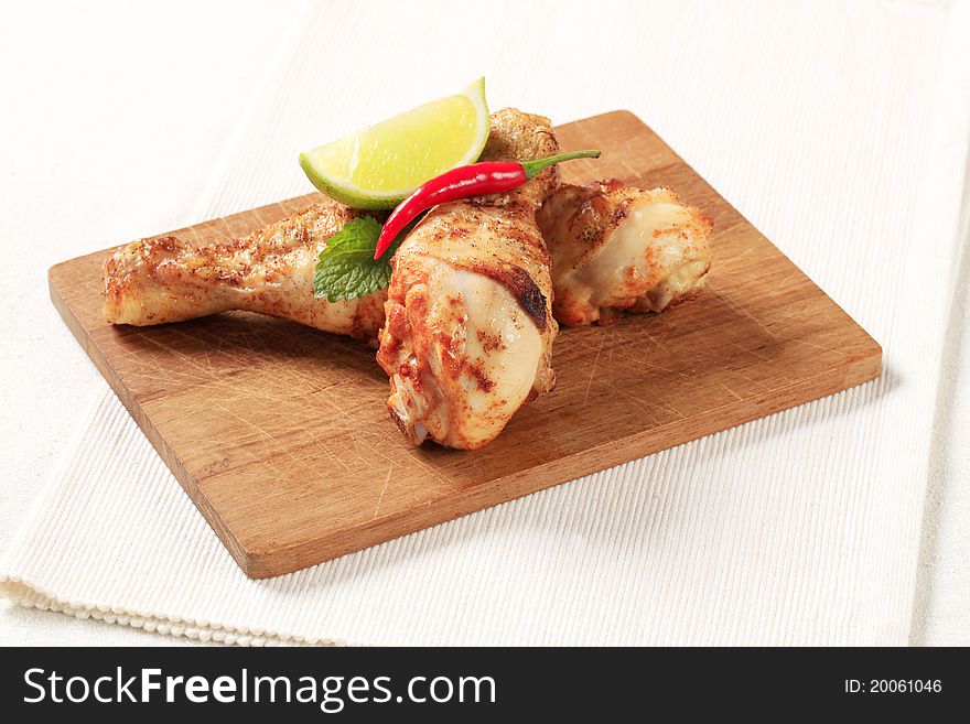 Two roasted chicken drumsticks on a cutting board