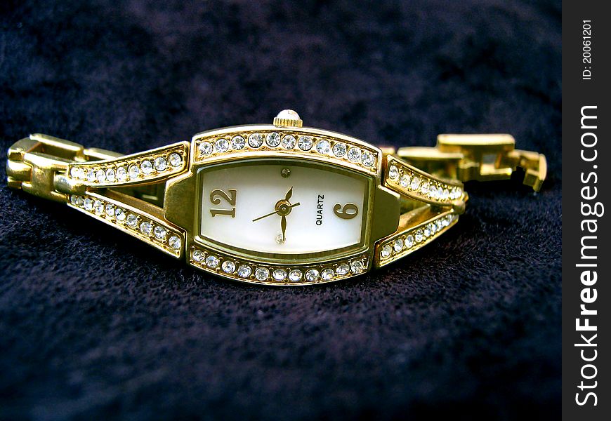 A golden ladies watch on top of black seude material.