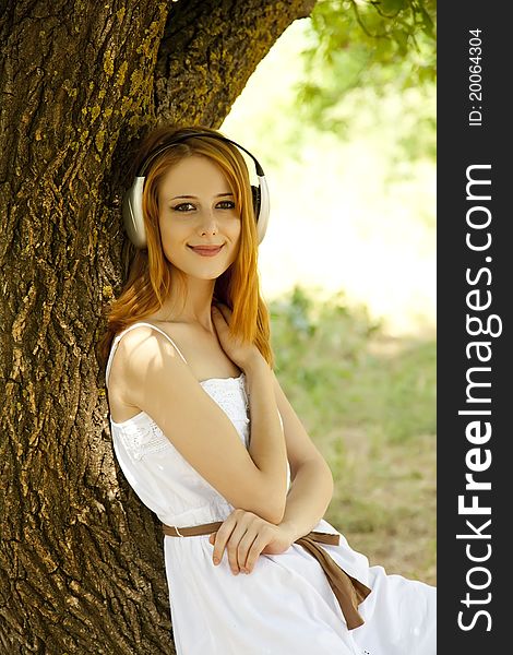 Beautiful redhead girl with headphones at garden.