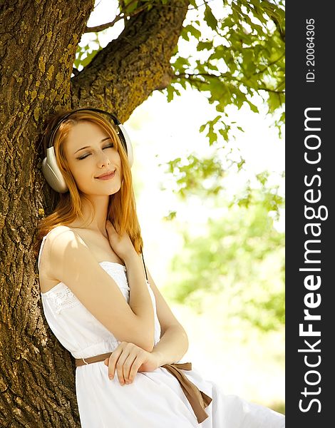 Beautiful redhead girl with headphones at garden.