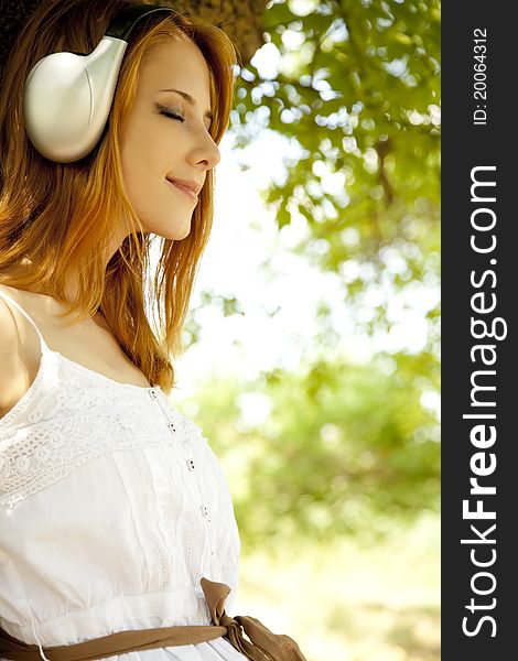 Beautiful redhead girl with headphones at garden.