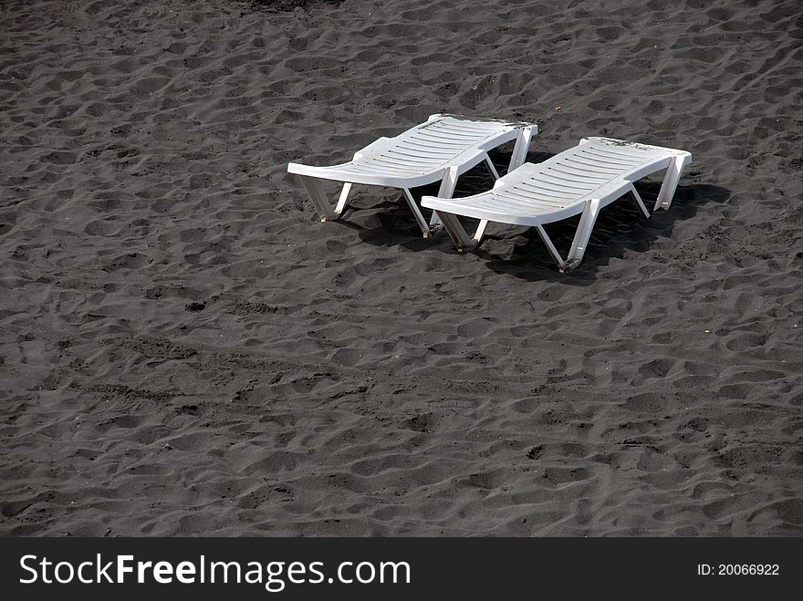 Image of 2 lounge plastic white beds on black sand beach of la Palma, Canary