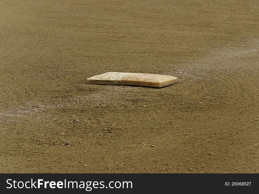 A lone baseball plate on a well maintained baseball field showing a faint white marker.