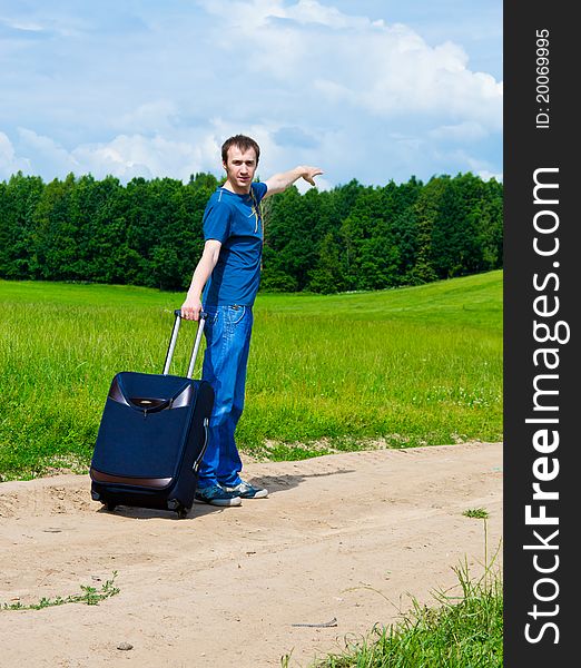 The young man on road in field with a suitcase