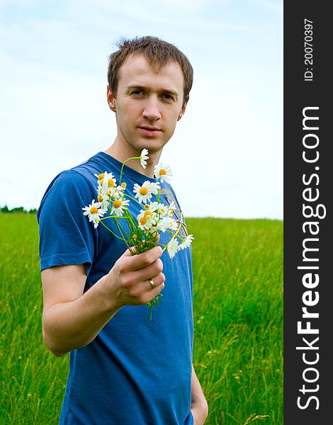 The young man with camomiles on green meadow