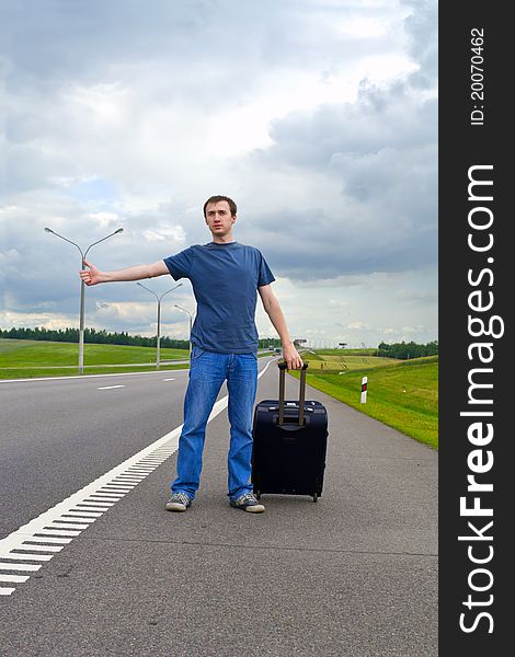 The young man pending on road with a suitcase